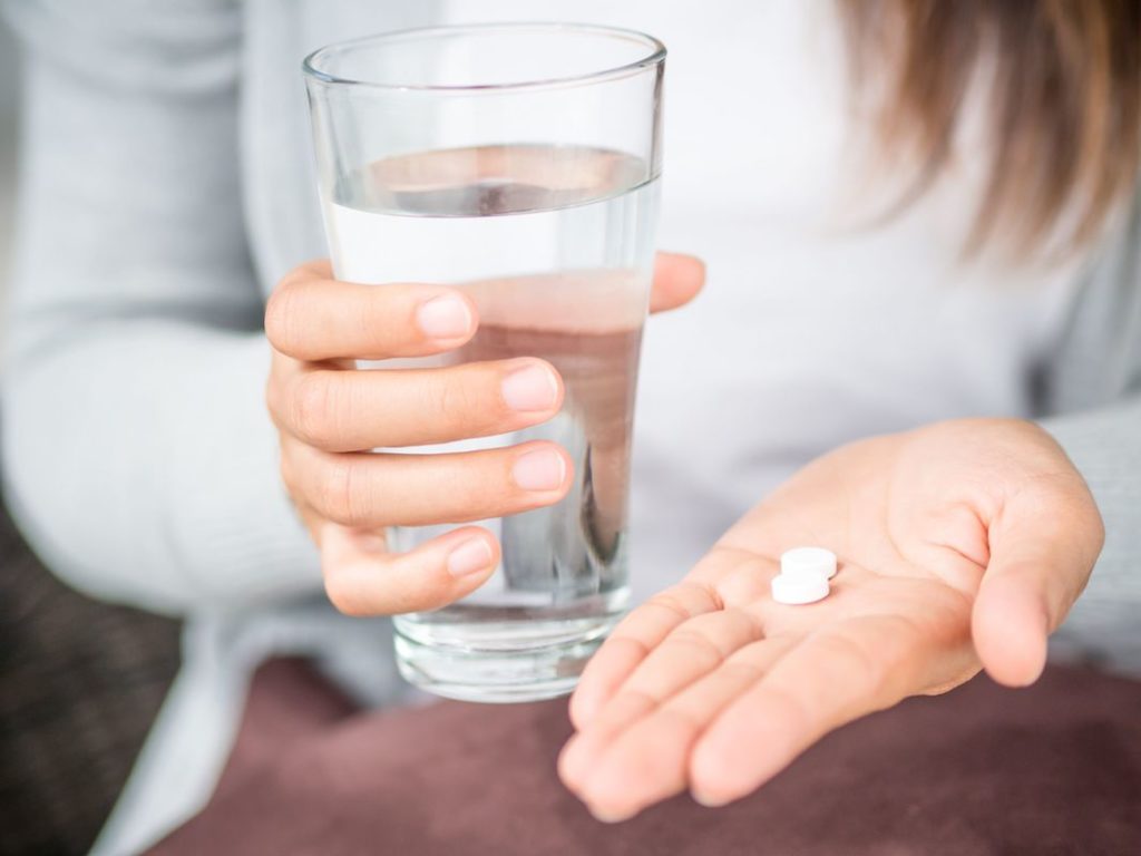 woman holding white pill tablets in hand with glass of water