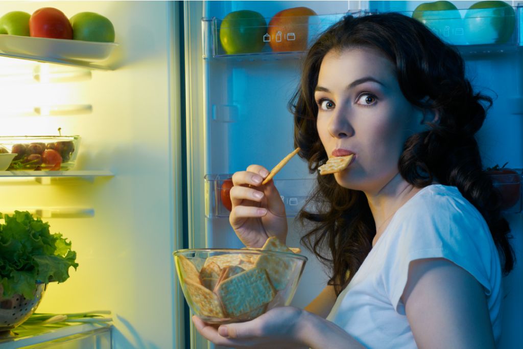 Woman by her fridge eating a late night snack of crackers