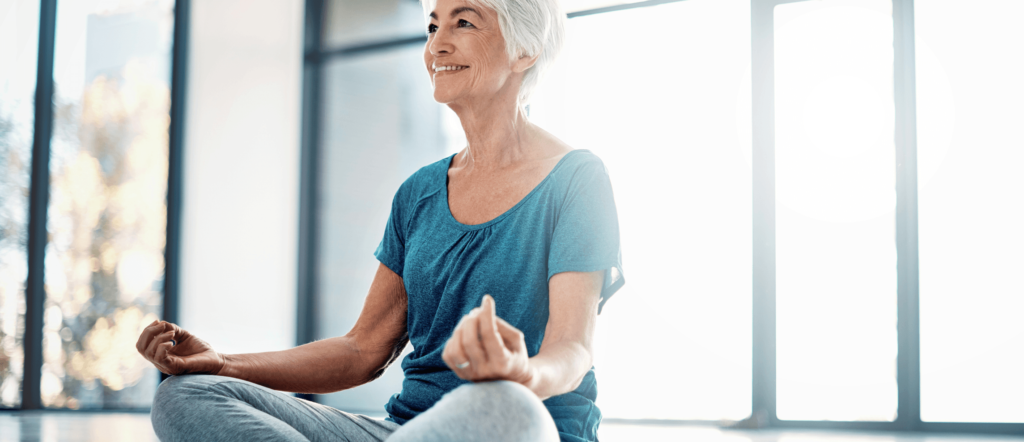 older woman smiling and sitting in yoga pose