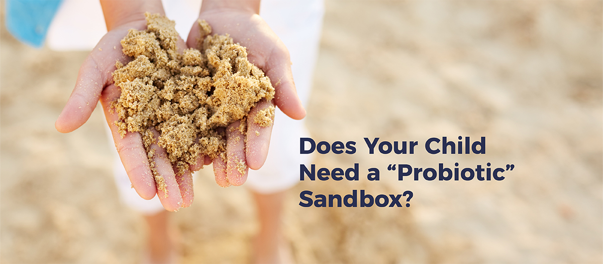 Close up of a woman's hand holding sand on a beach. Text reads "Does Your Child Need A Probiotic Sandbox?"