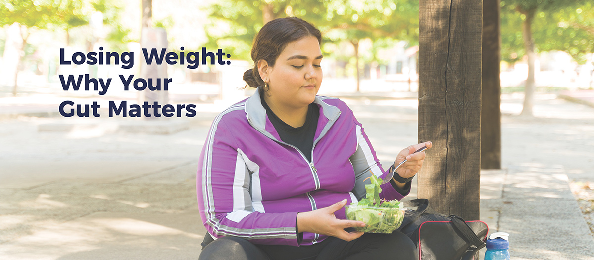 Young woman in running clothes sitting down outside and easting a salad. Text reads "Losing weight: why your gut matters".