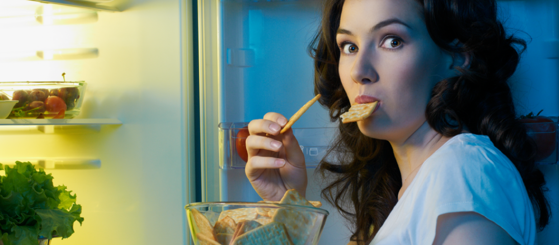 Woman by her fridge eating a late night snack of crackers