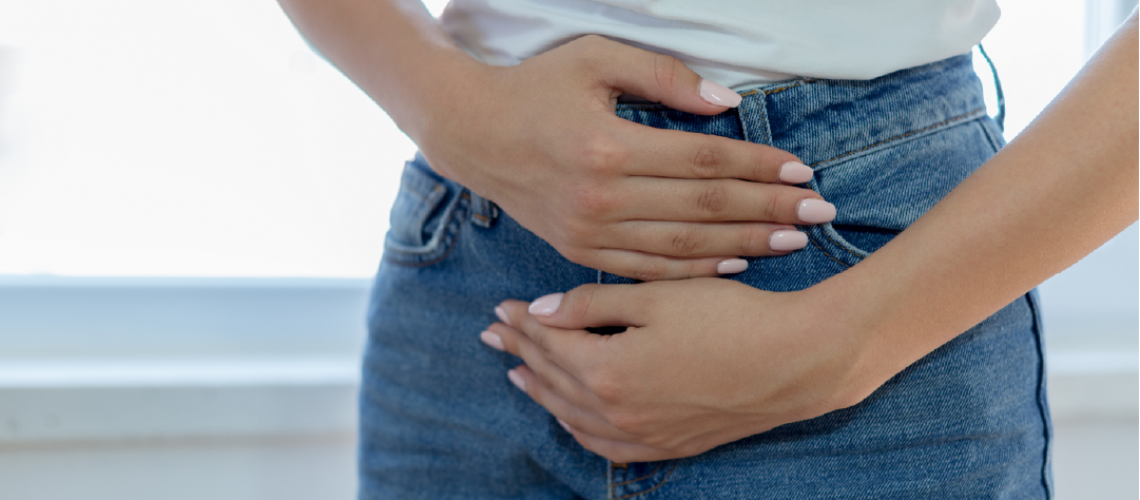 Woman in white shirt and jeans holding her upset stomach