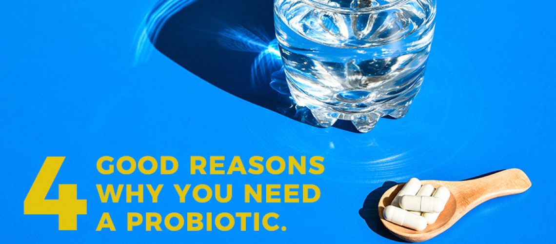 Five capsules on a wooden measuring spoon next to a glass of water. Text: 4 Good reasons why you need a probiotic