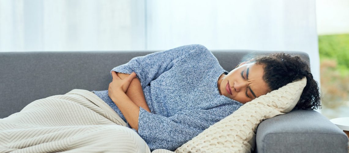 woman laying on couch holding stomach in pain from fibromyalgia and IBS