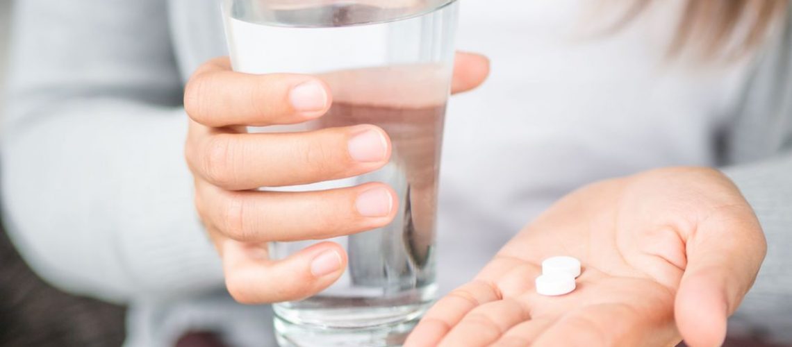 woman holding white pill tablets in hand with glass of water